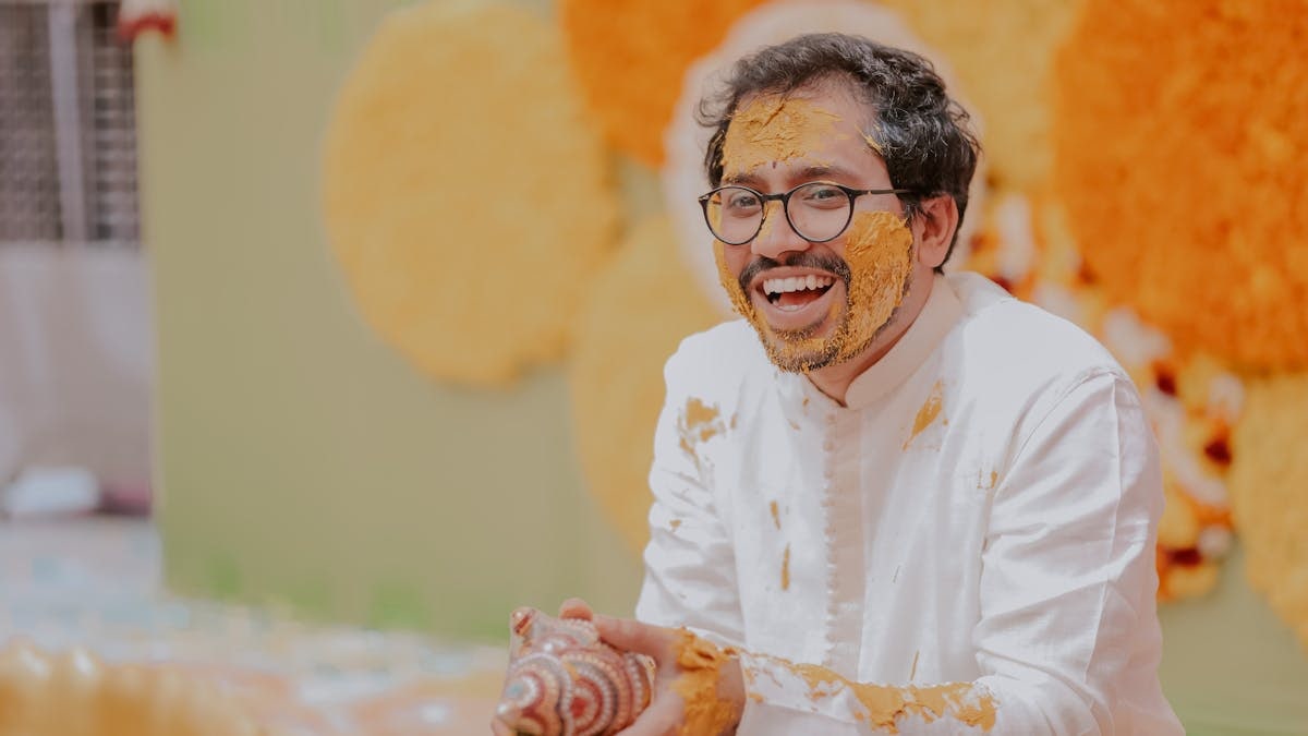 Happy Indian man laughing during traditional Haldi ceremony, covered in turmeric.